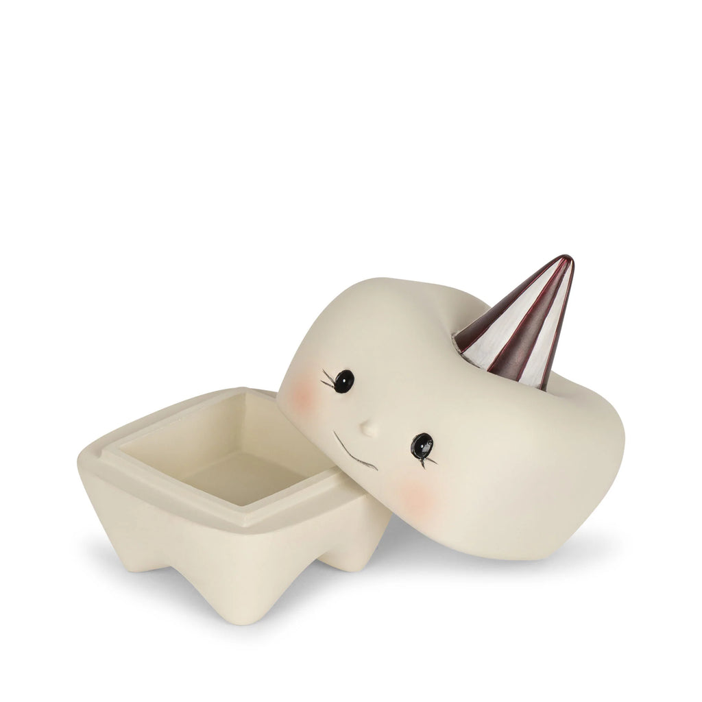 A small, square-shaped ceramic container with four legs is designed to resemble a cute tooth with a smiling face. Ideal as the Konges Sløjd Stone Tooth Box for your child's first teeth, the removable lid is adorned with a shiny silver cone resembling a party hat, and the container itself is open, showing its empty interior.