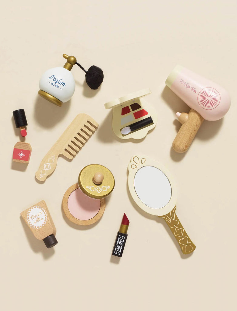 Flat lay of the Vanity Star Beauty Kit, featuring a wooden perfume bottle, hair dryer, mirror, blush, lipstick, nail polish, and comb—ideal for imaginative role-play—arranged on a light beige background.