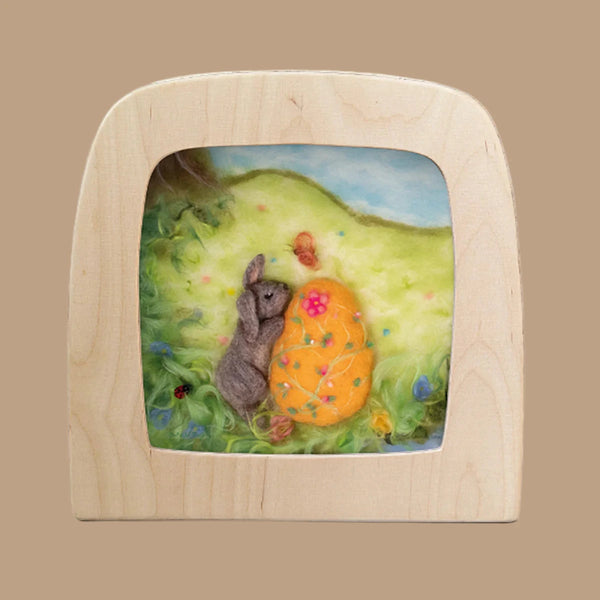 A needle-felted scene called "Silhouette Only - Easter Bunny for Toverlux Lamp" showcases a gray rabbit and a large yellow mushroom with flowers against a blue sky. Framed in light wood, the artwork is set on green grass with a charming ladybug accentuating the tableau.