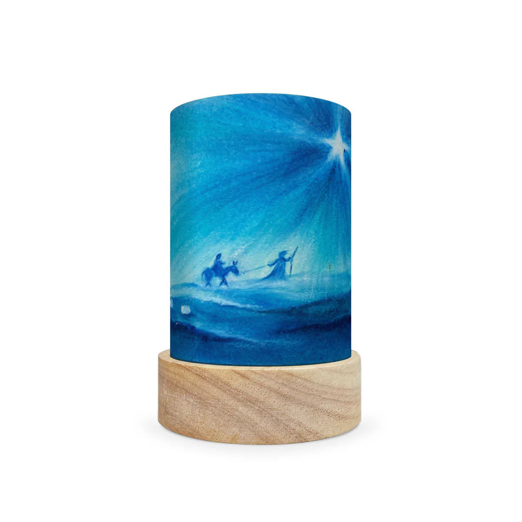 The Toverlux Lantern Shade Set - Holidays, with a stunning blue, starry sky design and magical shades, showcases silhouettes of two figures on a journey, one riding a donkey. This exquisite candle is elegantly displayed on a wooden base.