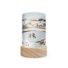 The Toverlux Lantern Shade Set - Robin Pieterse captivates with a winter scene, featuring two people ice skating on a frozen pond. Snow-draped hills and houses create the backdrop, all beautifully depicted on this cylindrical lamp. It rests elegantly on a wooden base, enhancing its charm with magical silhouettes.