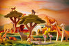 A colorful diorama depicts a vibrant sunset scene with various handcrafted wooden toys by Ostheimer, including elephants, lions, zebras, giraffes, monkeys, a parrot, and flamingos. The backdrop features an Ostheimer African Tree alongside felt trees and a wavy, multicolored landscape perfect for imaginative play.