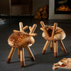 Two unique wooden Faux Bambi Chairs with faux fur seats, designed to resemble deer, are positioned on a sleek floor near a lit fireplace, with logs and a board game nearby, creating a cozy atmosphere.