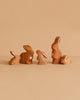 The Bumbu Handmade Wooden Brown Bunny Rabbit Family Set features five small, brown bunny figurines with white spots and heart details, arranged in a row on a beige background—ideal for Montessori toy collections.