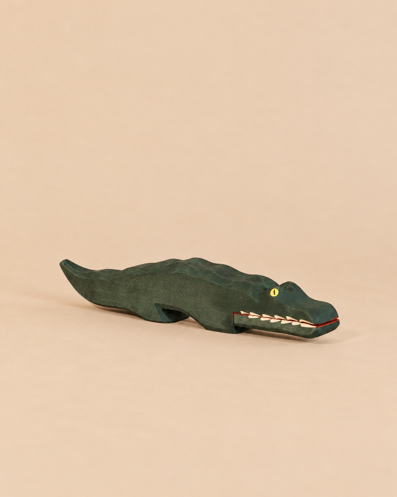 An Ostheimer Crocodile handcrafted wooden figure painted dark green with a yellow eye and visible white teeth, perfect for imaginative play.