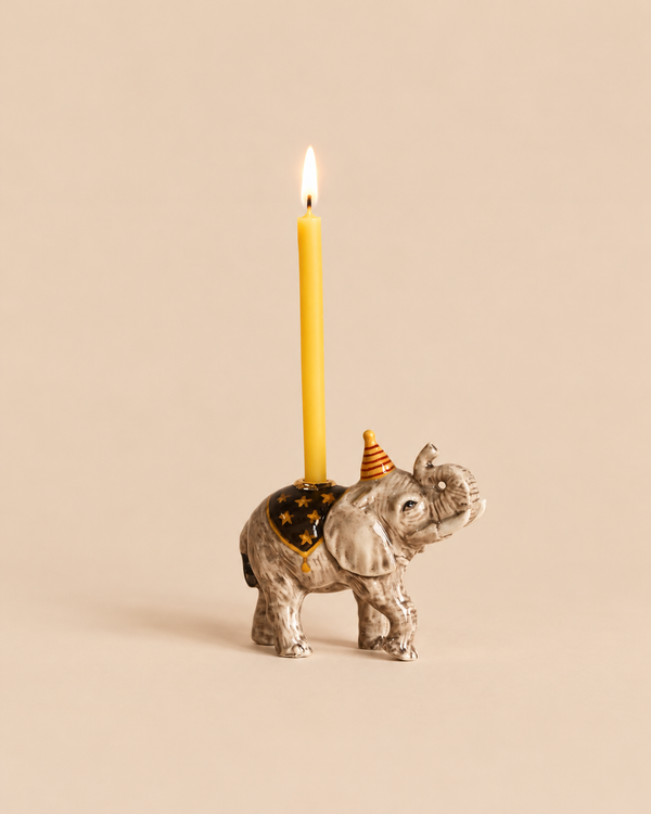 Elephant Cake Topper - Final Sale featuring a ceramic elephant wearing a party hat and a star-patterned blanket, holding a lit yellow taper candle on its back as a handcrafted collectible birthday decoration.