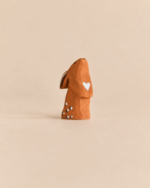 A Bumbu Handmade Wooden Curious Rabbit, featuring a brown finish with a white heart on its chest and white spots on its back, perfect for an Easter basket.