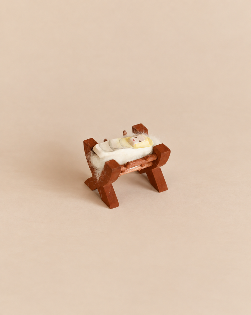 An Ostheimer Baby In Crib featuring a handcrafted wooden figurine of a baby wrapped in white cloth resting in a wooden crib.