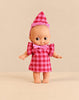 A Minikane Mini Pancha Doll - Ninon Celebrating with Cherry Gingham Outfit, featuring a vinyl doll in a pink and red gingham dress, a matching cone-shaped party hat with ruffled trim, and a pink neckline bow.