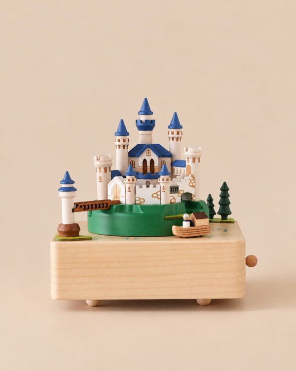 The Forest Castle Music Box features a castle with blue turrets, a small bridge, and a boat on a rotating green platform.