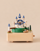 The Forest Castle Music Box features a castle with blue turrets, a small bridge, and a boat on a rotating green platform.