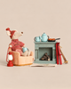 A Maileg Winter Chalet Set featuring a winter ski mouse in a knit sweater and hat sitting in an armchair with a mug, beside a fireplace with a tea set, food, a red lantern, and a pair of skis.