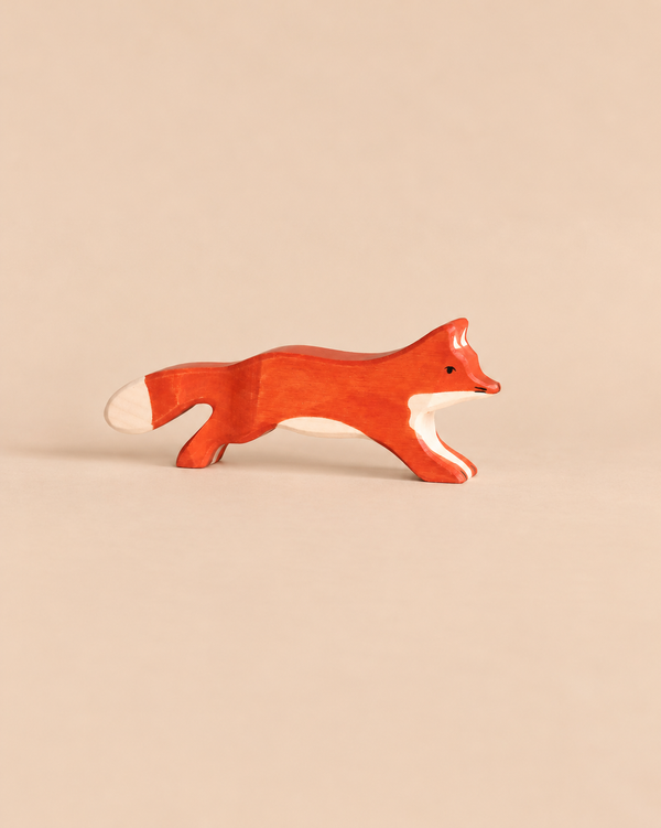 A Holztiger Running Fox handcrafted wooden toy, painted orange with white accents on its face, chest, and tail in a running pose.