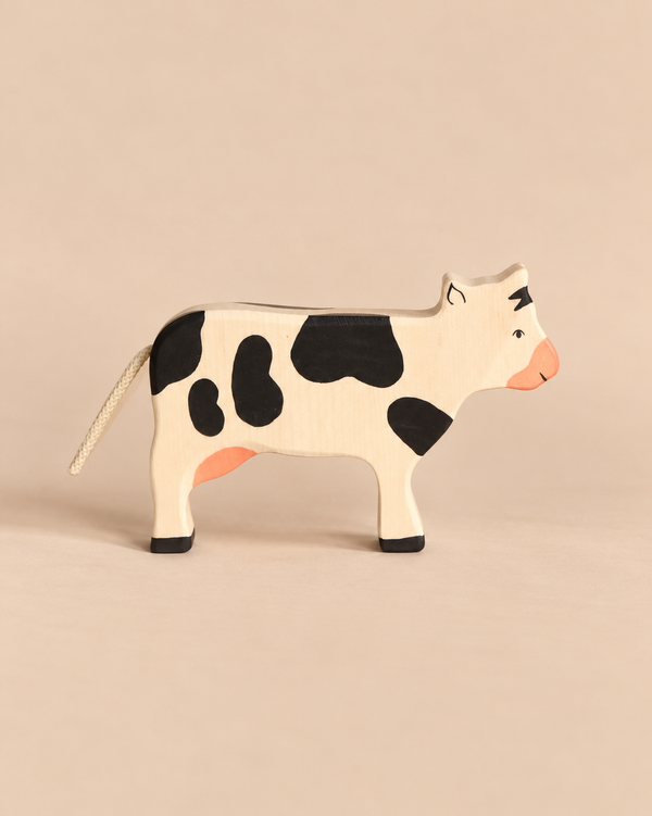 Holztiger Black Cow, Standing, a handcrafted wooden toy with black spots and a rope tail, shown in profile.