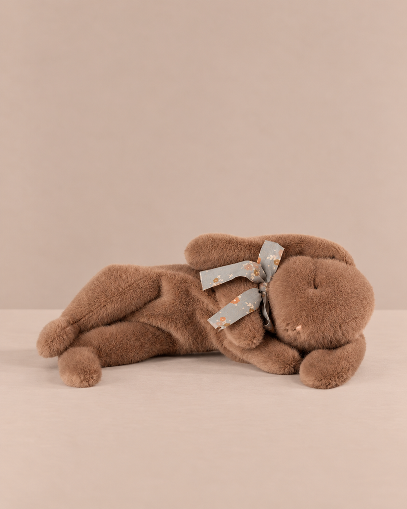 A soft brown Maileg Plush Sleeping Bunny lying on its side, wearing a small floral bow around its neck.