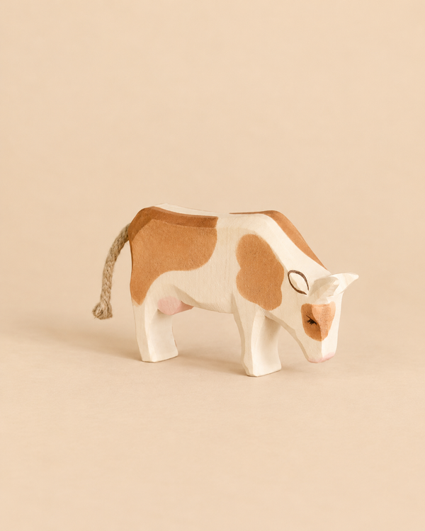 Handcrafted Ostheimer Cow - Eating, a wooden toy with brown patches, head bowed as if grazing, and a braided rope tail.