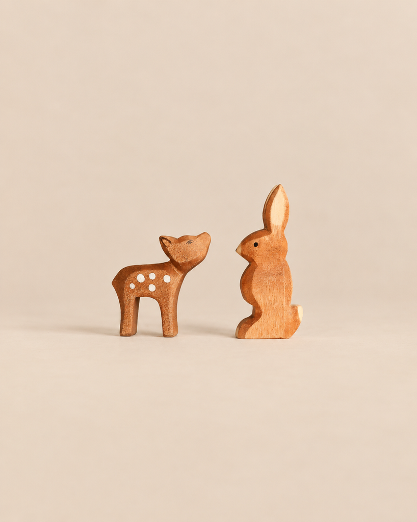 An Ostheimer Handmade Wooden Woodland Set featuring a handcrafted wooden fawn and rabbit facing each other.