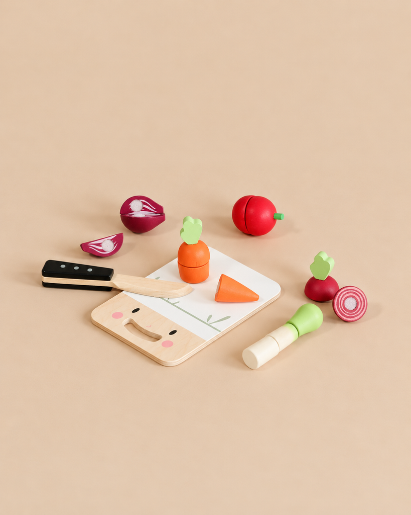 Mini Chef Chopping Board featuring a sustainable rubber wood cutting board, a wooden knife, and toy fruit and vegetables including a carrot, onion, and beet.