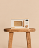 A wooden Pretend Play Microwave with a rattan door panel and wooden handle, sitting on a wooden stool as part of a play kitchen.