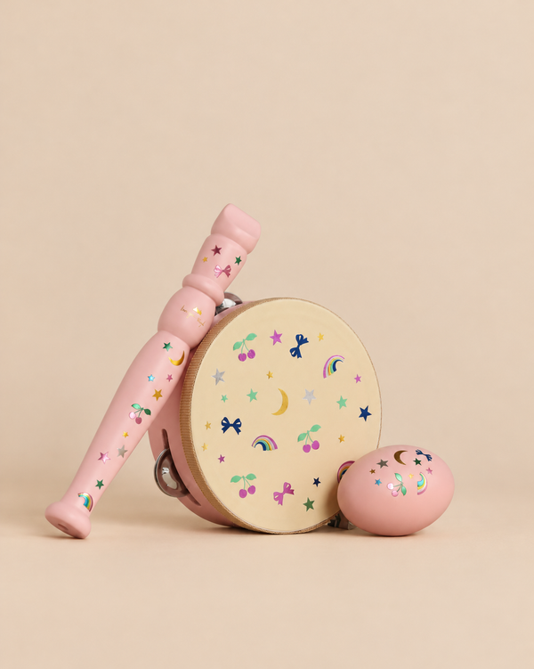 The Konges Sloejd Music Set Petite - Rainbow Twinkle includes a pink wooden maraca, a tambourine, and an egg shaker, all decorated with colorful stickers of cherries, stars, moons, bows, and rainbows.