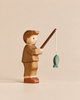 A handmade Holzwald Fishing Pond Set figurine of a person wearing a cap, holding a fishing rod with a small blue fish hanging from the line.