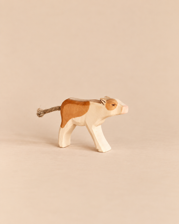 Ostheimer Calf - Drinking: a handcrafted wooden toy calf with brown patches and a rope tail, shown in a standing, lowered-head position.