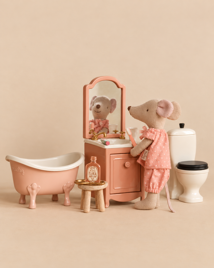 A Maileg Big Sister Bathroom Set features a Big Sister Mouse in pink polka-dot pajamas standing at a miniature vanity with a toothbrush, next to a pink clawfoot bathtub and a toilet.
