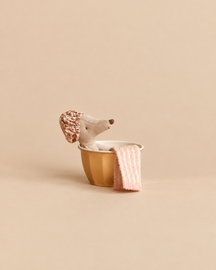 A Maileg Wellness Mouse, Big Sister (Rose) wearing a floral shower cap sits in a small yellow basin with a striped towel draped over the side.