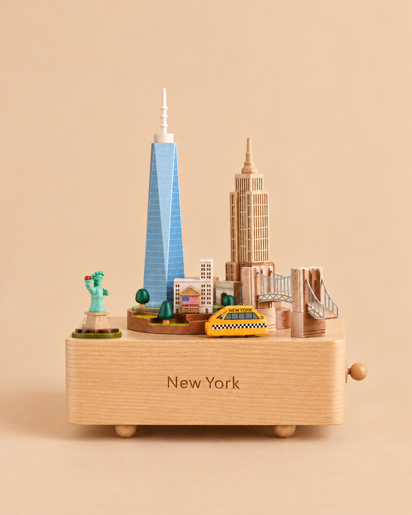 Wooden New York Music Box featuring miniature landmarks including the Statue of Liberty, One World Trade Center, the Empire State Building, the Brooklyn Bridge, and a yellow taxi, with “New York” engraved on the front base.