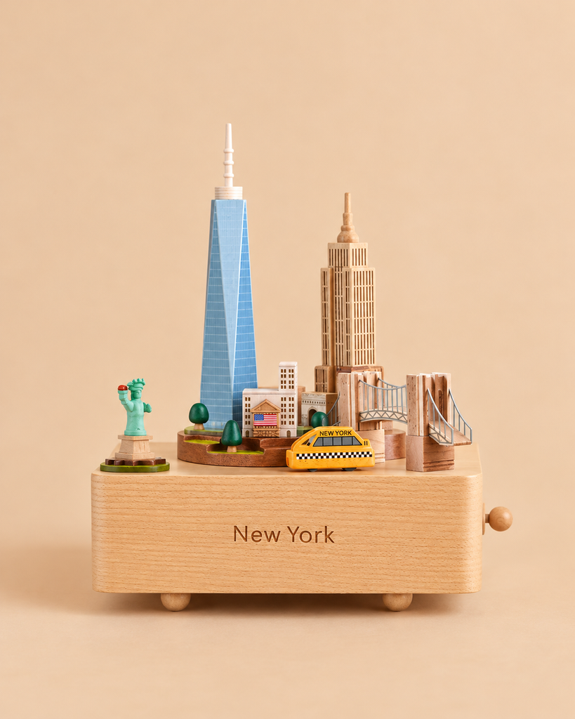 Wooden New York Music Box featuring miniature landmarks including the Statue of Liberty, One World Trade Center, the Empire State Building, the Brooklyn Bridge, and a yellow taxi, with “New York” engraved on the front base.