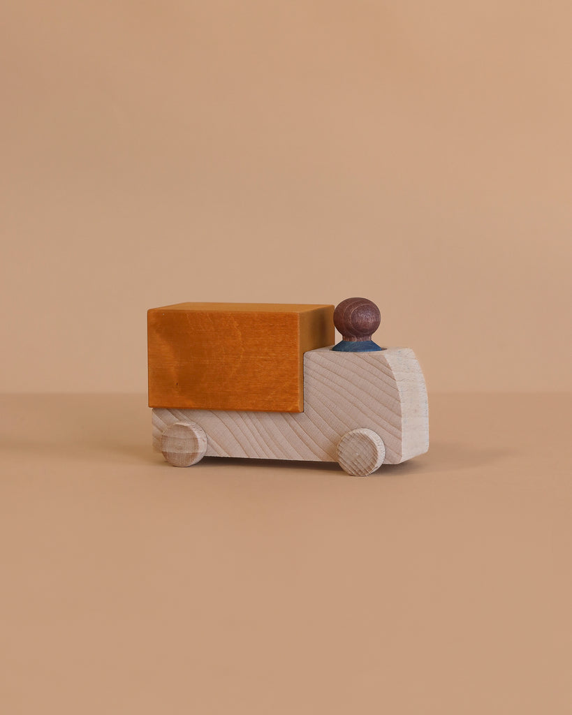 The Lubulona Wooden Truck - Ochre features a simple wooden design with a rectangular ochre cargo section and a small dark wooden driver—ideal for fans of sustainable toys.