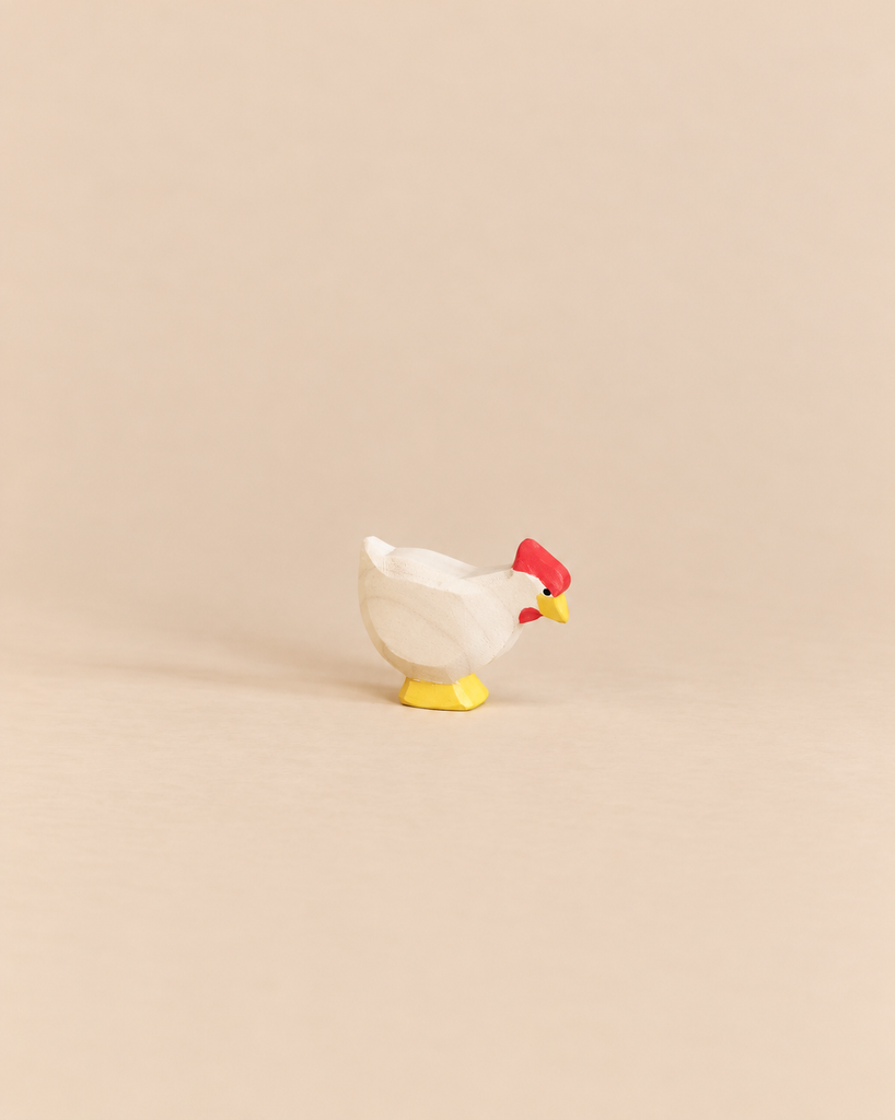 An Ostheimer White Hen - Standing handcrafted as a small wooden toy with a white body, red comb, and yellow feet, perfect for imaginative play.