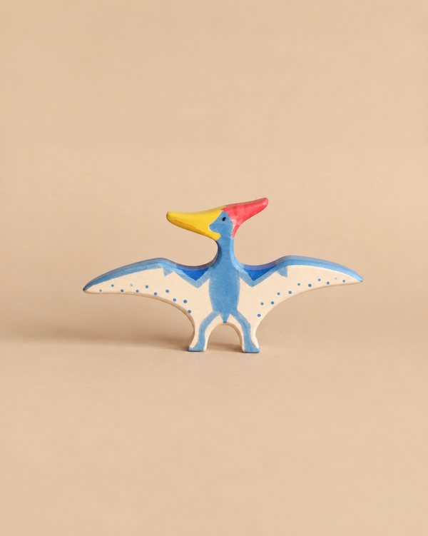 Holztiger Pteranodon dinosaur toy handcrafted in wood, painted blue with a yellow beak, red crest, and blue polka dots on its wings.