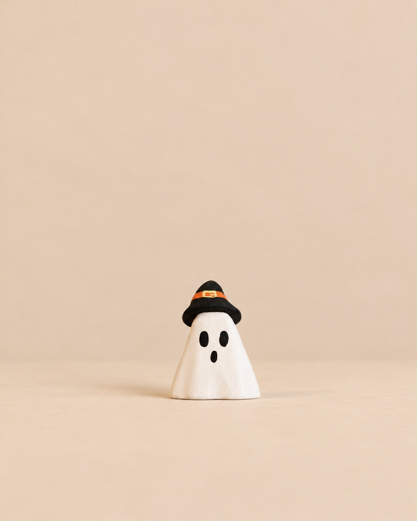 A small ghost figurine from the Bumbu Handmade Wooden Halloween Friends Set, wearing a black witch hat with an orange band, perfect for small world play.