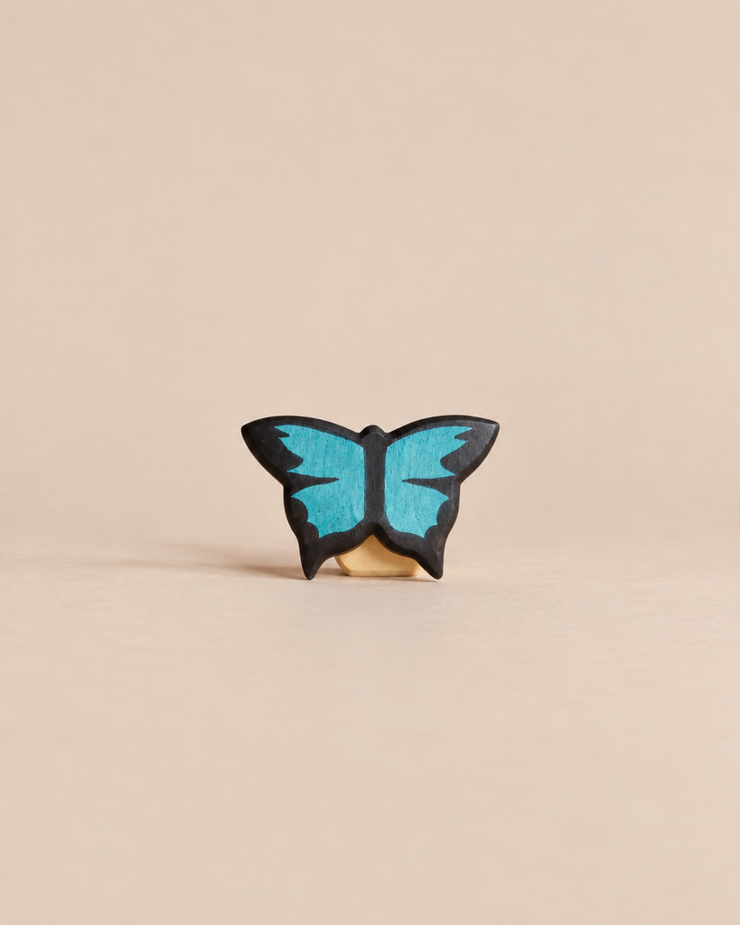 Handmade Holzwald Butterfly, a small, sustainable wooden figurine with black wings featuring bright blue details for imaginative play.