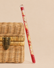 Konges Sloejd Magical Glitter Wand - Cherry filled with red beads and gold star-shaped glitter, leaning against a small woven basket.