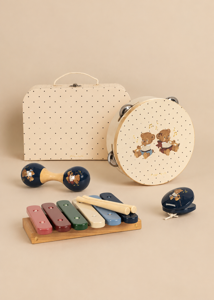 A Konges Sloejd Music Set - Teddy Bear featuring a xylophone with mallets, a maraca, a tambourine, and castanets with teddy bear illustrations, arranged in front of a dotted storage suitcase.