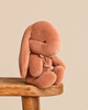 Maileg Plush Bunny, Medium - Vintage Rose sitting on a wooden stool, featuring long ears and a small ribbon around its neck.