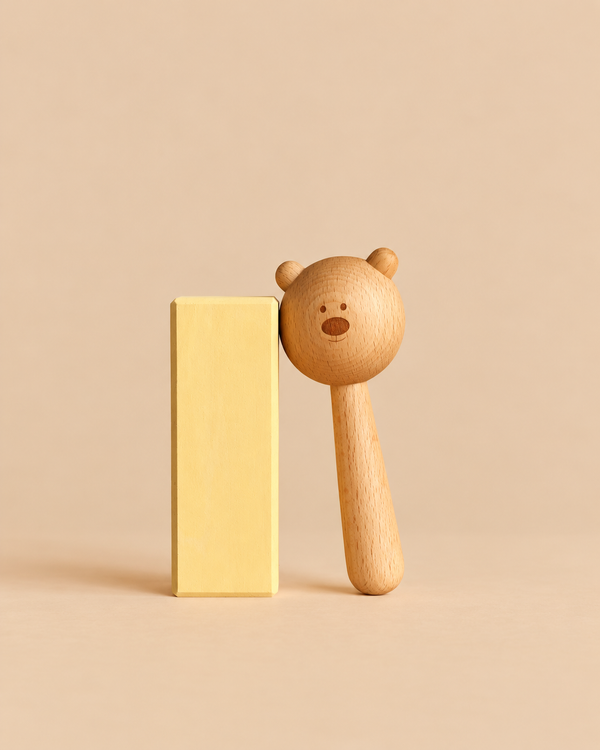 A natural Sabo Concept Bear Rattle - Natural leaning against a tall, pale yellow rectangular block.