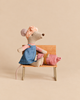 A Maileg Hiker Mouse With Blush Sleeping Bag - Big Sister sits on a miniature wooden bench, wearing a headscarf and denim overalls next to a small, rolled-up sleeping bag.