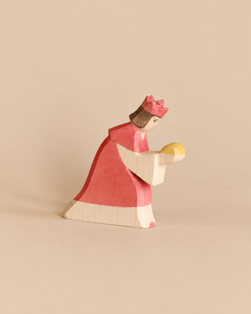 Ostheimer Red King With Crown: a handcrafted wooden toy figure of a king in a red robe and crown, kneeling and holding a yellow orb for imaginative play.