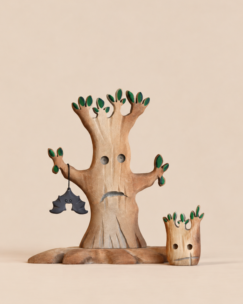 A Bumbu Handmade Wooden Halloween Trees With Hanging Bat set featuring a sad-faced tree with green-tipped leaves and a black bat, standing beside a smaller, matching wooden tree stump figure.