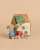 Two Maileg mice in striped shirts and shorts sit in front of a small cardboard house featuring a Maileg Garden Tea Set and other furniture.