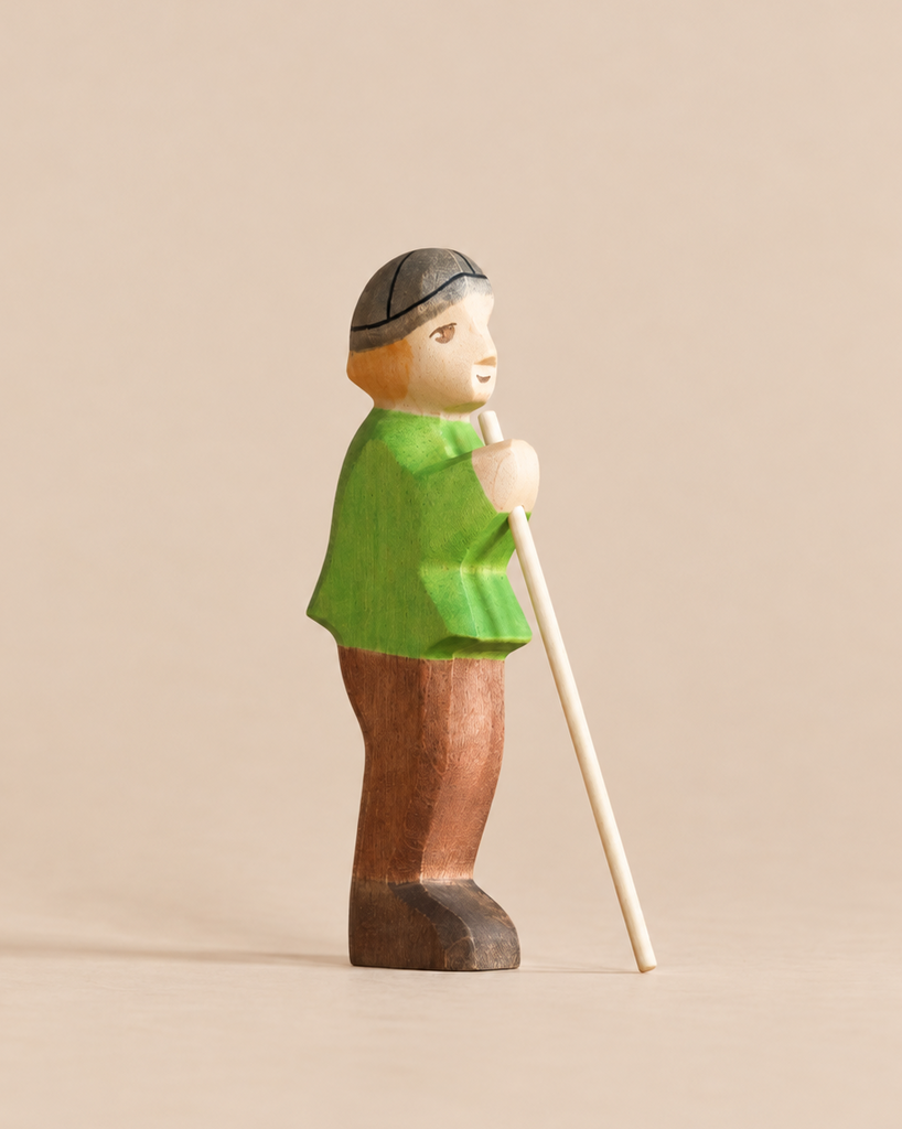 Handmade Holzwald Shepherd & Farm Animals Set shepherd figurine in a green shirt and brown pants holding a long staff.