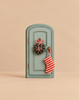 A miniature sage green Maileg Christmas Mice Set door, arched and decorated with a small wreath tied with red-and-white twine and a hanging red-and-white striped stocking.