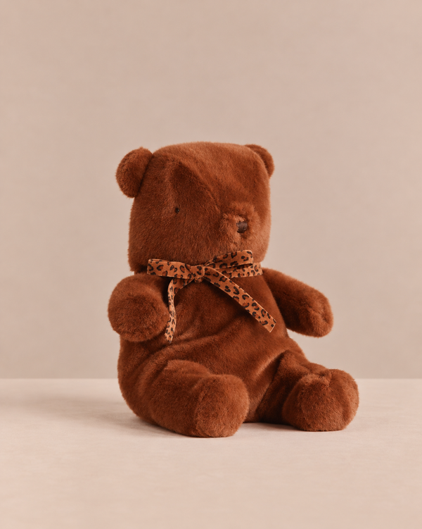 A medium brown Maileg Teddy Bear Plush, Medium - Dark Chocolate wearing a leopard print ribbon around its neck.