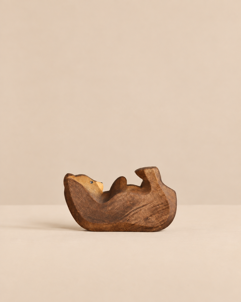 A small, hand-carved wooden Handmade Holzwald Bear Cub - Lying resting on its back, perfect for imaginative play.