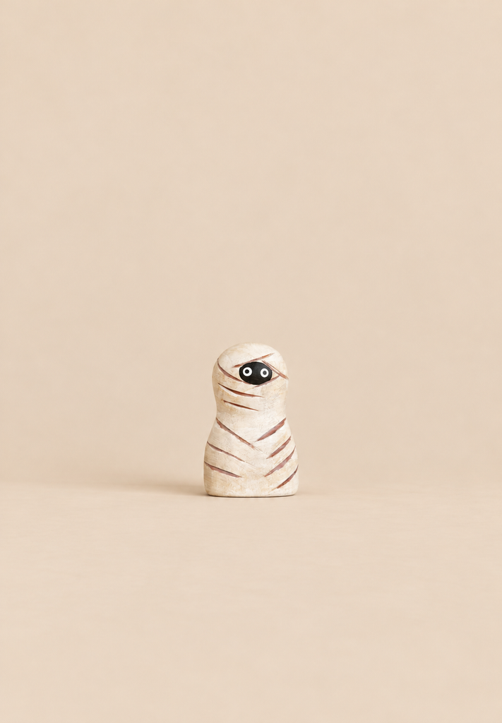 A small mummy figurine from the Bumbu Handmade Wooden Halloween Friends Set, featuring carved wrappings and two black eyes, perfect for small world play.