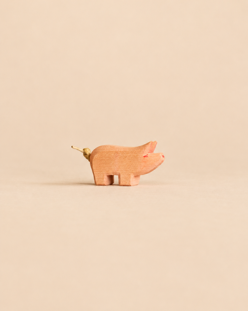 Small handcrafted wooden Ostheimer Piglet figurine with a knotted string tail, perfect for imaginative play.