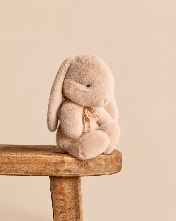 Maileg Plush Bunny, Small - Latte, a plush tan stuffed animal with long ears sitting on a wooden stool.
